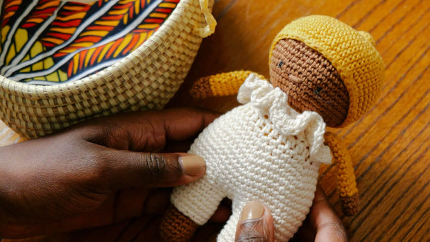 Yellow-hatted La Petite Senna in white dungarees, featuring a matching white basket cot, pillow, mattress, and duvet