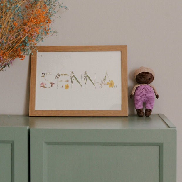 Charming La Petite Senna with a mocha hat and lilac dungarees, showcased with a white basket cot, pillow, mattress, and duvet 