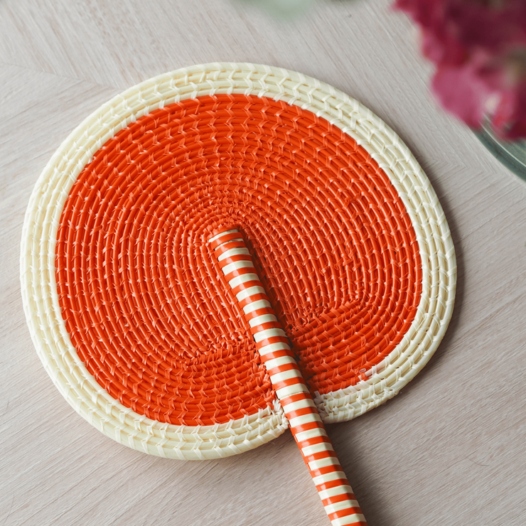 La Basketry handwoven fan in cream and orange placed on a wooden table