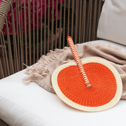 La Basketry handwoven fan in orange and cream on a cream blanket 