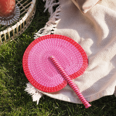 La Basketry pink and red woven fan on a cream blanket in the grass
