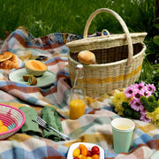 La Basketry picnic basket in natural woven basket with a yellow stripe shown on a tartan blanket with picnic food and drink