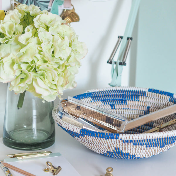 la basketry handwoven storage bowl in blue and white pattern shown  on a desk with stationery and flowers