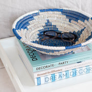 la basketry handwoven storage bowl in blue and white pattern shown on a tray with books