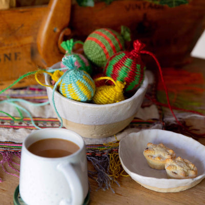 a bowl of colourful Christmas baubles woven with twine set on a table with mince pies and a cup of tea  as part of the Weave Your Own Christmas Baubles Kit by la basketry