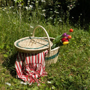 La basketry handwoven green picnic basket on a green field with a stripey blanket and a bouquet of tulips