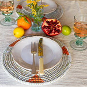 La Basketry orange and white handwoven placemat set on a dining table with some citrus, lemons and oranges on a linen tablecloth