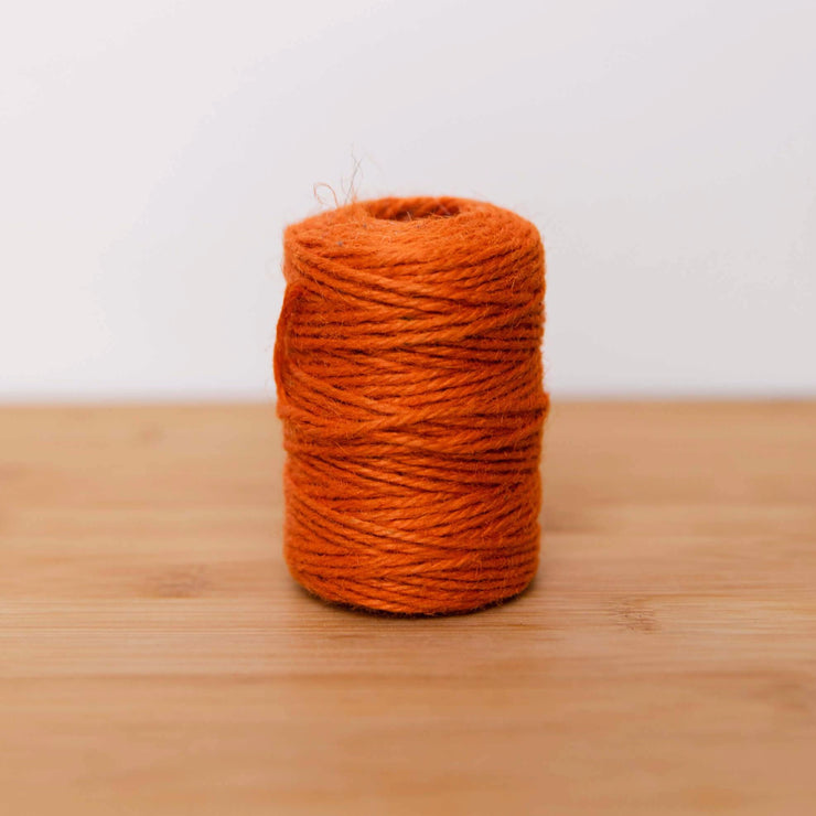 La Basketry roll of orange twine for basket weaving on a wooden surface against a white  background 