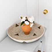 La Basketry Woven Serving Tray with a triangle pattern on a console with a bouquet of white flowers