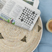 La Basketry woven serving tray with a triangle pattern against a blue tablecloth with a cup of coffee and newsletter