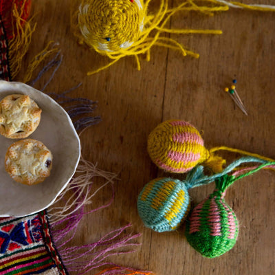 a set of three Christmas baubles woven with colourful twine set on a wooden  table next to some mince pies  as part of the  Weave Your Own  Christmas Baubles by La Basketry