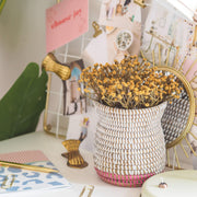 la basketry handwoven vase in white and pink weave with yellow flowers, shown on a desk with stationery