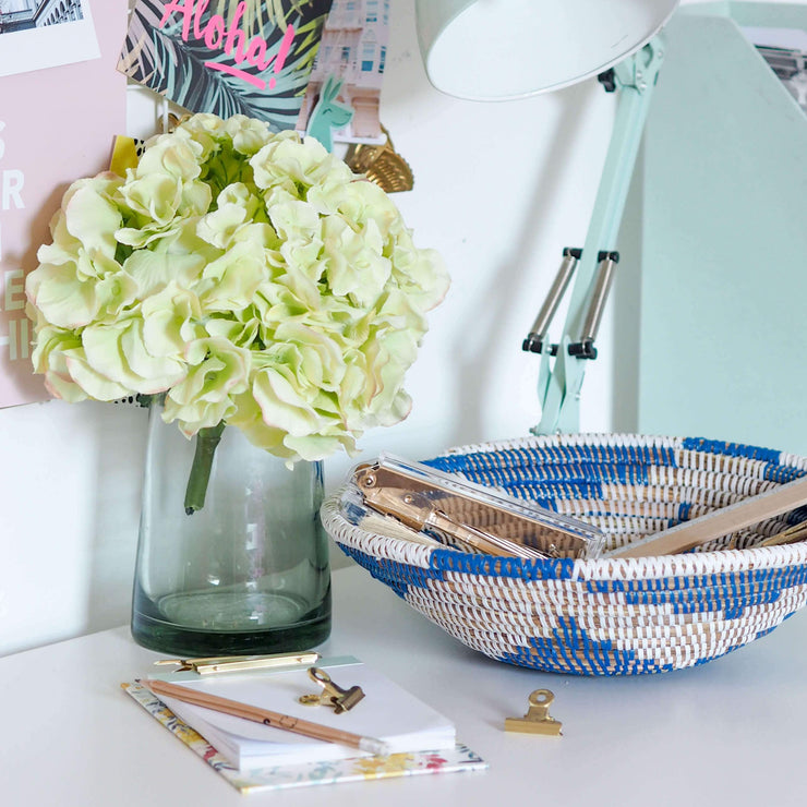 la basketry handwoven storage bowl in blue and white pattern shown on a desk with stationery and flowers