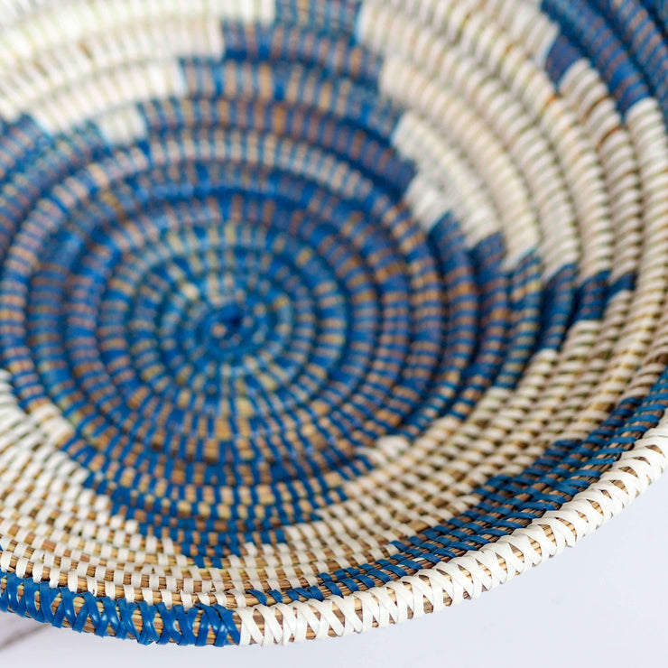 la basketry handwoven storage bowl in blue and white pattern shown close up highlighting the weave of natural grasses and plastic strips